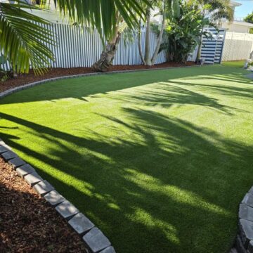 Sunny curved shape backyard with artificial turf, bordered by chsrcoal coloured windsor blocks as garden edging.